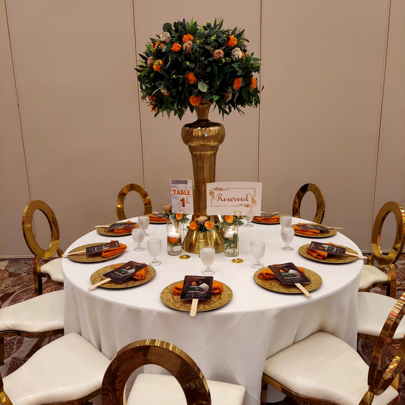 Round reception table styled in white, gold and orange with a tall floral centerpiece
