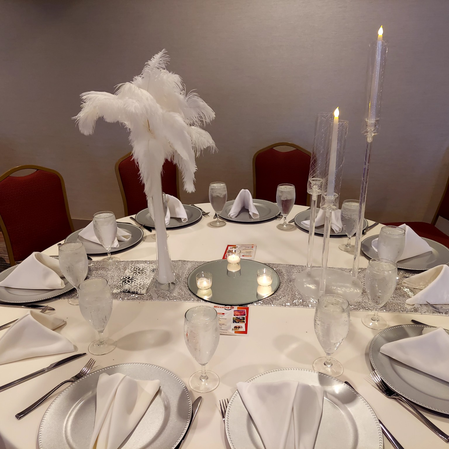 White and silver tablescape with feather centerpiece and tall clear candleholders