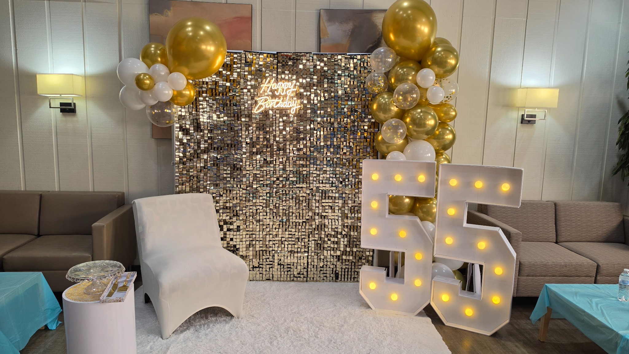 Gold and white 55th birthday balloon décor with a shimmering backdrop and illuminated numbers